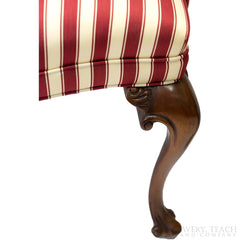 Close up on the cabriole style of the right leg of a striped parlor chair.