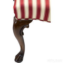 Close up on the cabriole style of the left leg of a striped parlor chair.
