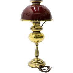 A vintage hurricane lamp with a dark red shade and golden base.
