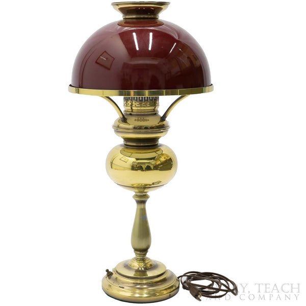 A vintage hurricane lamp with a dark red shade and golden base.